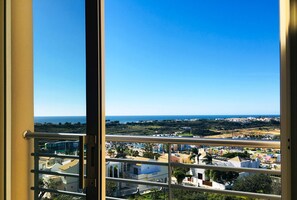 A view from a bedroom window overlooking a coastal town with buildings and greenery.