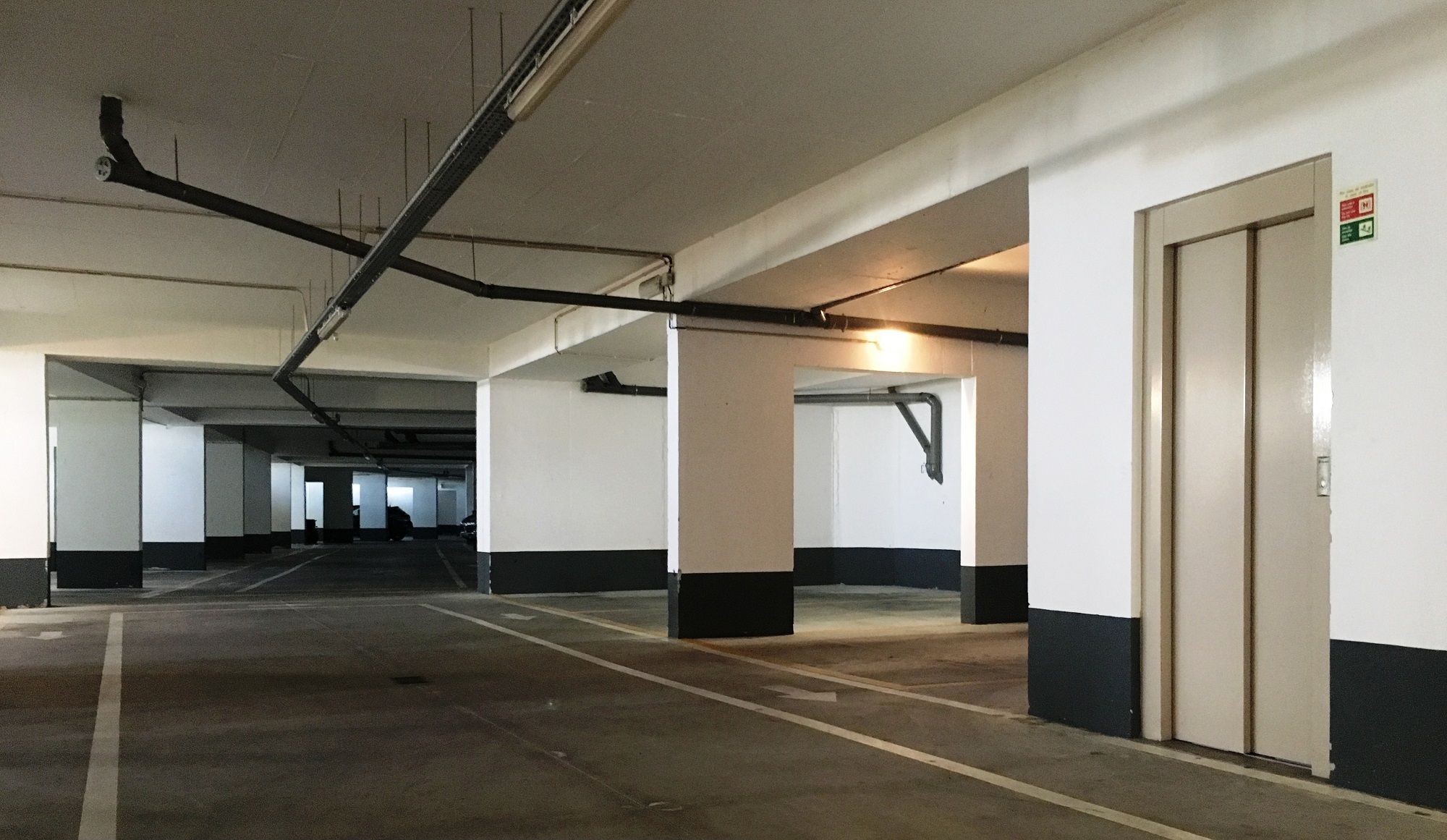 Garagem de estacionamento privativa sob os apartamentos, com piso de concreto e paredes brancas.