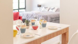 A dining table set with glasses, bowls, and plates, with a bed and pillows in the background. - Departamento en Bariloche con Terraza (San Carlos de Bariloche)