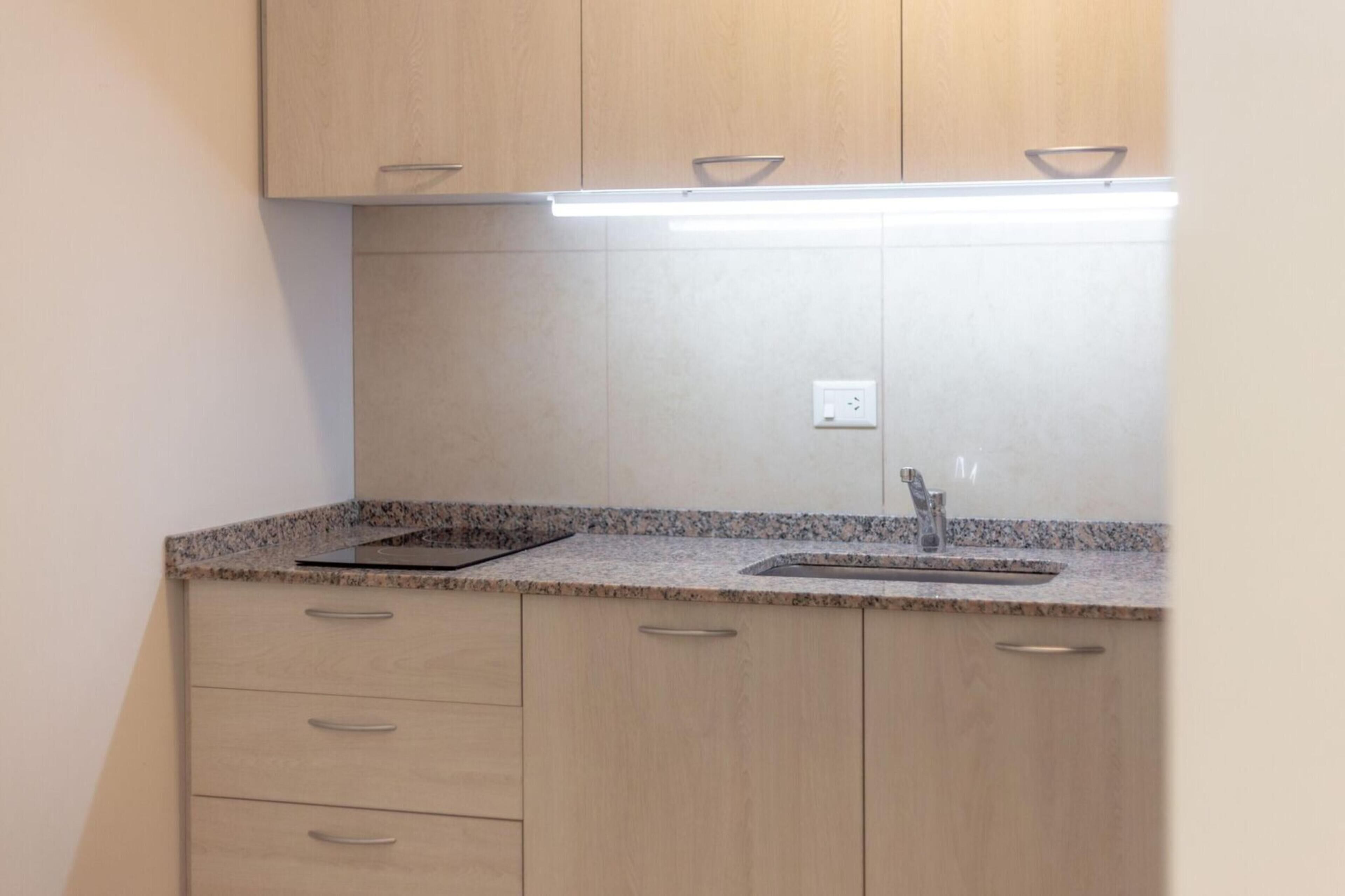 A kitchen with light wood cabinets, a granite countertop, and a stainless steel sink.