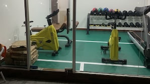Een sportschool met fitnessapparatuur, waaronder een geel apparaat, een spiegel die de ruimte weerspiegelt en een dumbbellsrek.