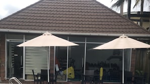 Een zwembad met twee parasols, een overdekt zitgedeelte en een gebouw met een betegeld dak op de achtergrond.