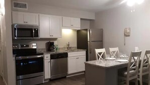 A modern kitchen with stainless steel appliances, white cabinetry, and a dining area with a marble countertop and four chairs. - Surf Suites (Wrightsville Beach)