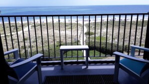 A balcony with a table and two chairs, overlooking a beach with a path and dunes. - Surf Suites (Wrightsville Beach)