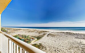 Blick auf einen Strand vom Balkon aus, mit blauem Himmel, sandigem Strand und etwas Vegetation.