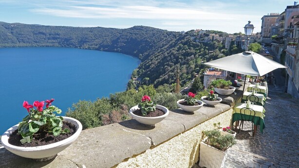 A terrace with potted plants and outdoor seating overlooking a lake and hilly landscape. - Vacation apartment Glicine - Vigna Luisa Resort - Close to Rome (Genzano di roma)