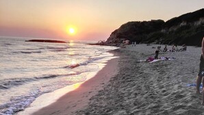 A beach with the sun setting over the horizon, people relaxing on the sand, and a rocky cliff in the background. - Vacation apartment Glicine - Vigna Luisa Resort - Close to Rome (Genzano di roma)