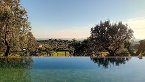 An infinity pool with clear water reflecting the surrounding landscape, surrounded by trees and a view of a distant town. - Vacation apartment Glicine - Vigna Luisa Resort - Close to Rome (Genzano di roma)