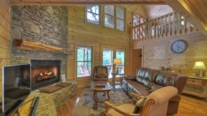 L’intérieur chaleureux d’un chalet avec une cheminée en pierre, des murs en bois, un canapé en cuir et un escalier en bois.