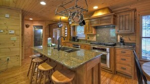 Une cuisine de style rustique, avec des meubles en bois, des comptoirs en granit, des appareils électroménagers en acier inoxydable et des tabourets en bois.
