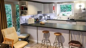 Una cocina moderna con armarios blancos, encimera negra y ventana con vistas a zonas verdes. Hay dos taburetes y una silla en la zona de estar.