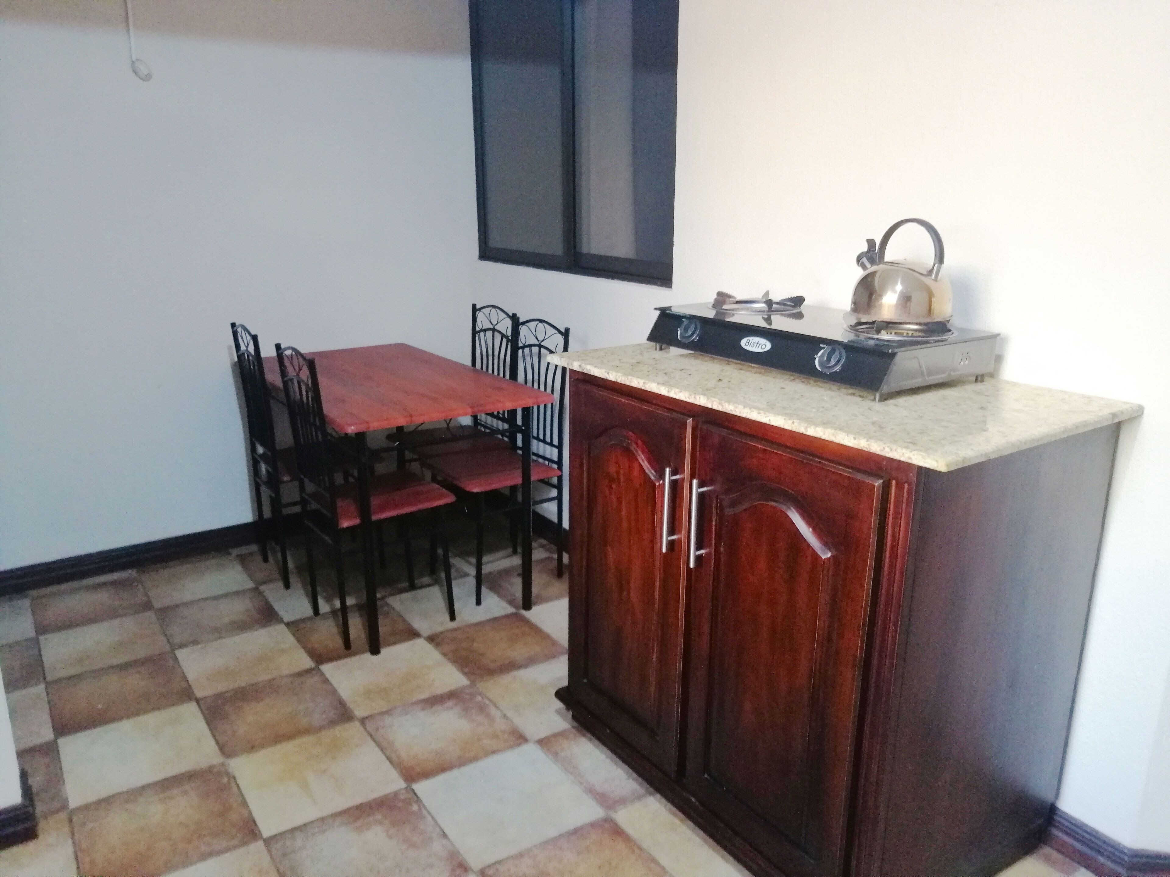 A kitchen with a gas stove, a kettle, and a dining table with chairs.