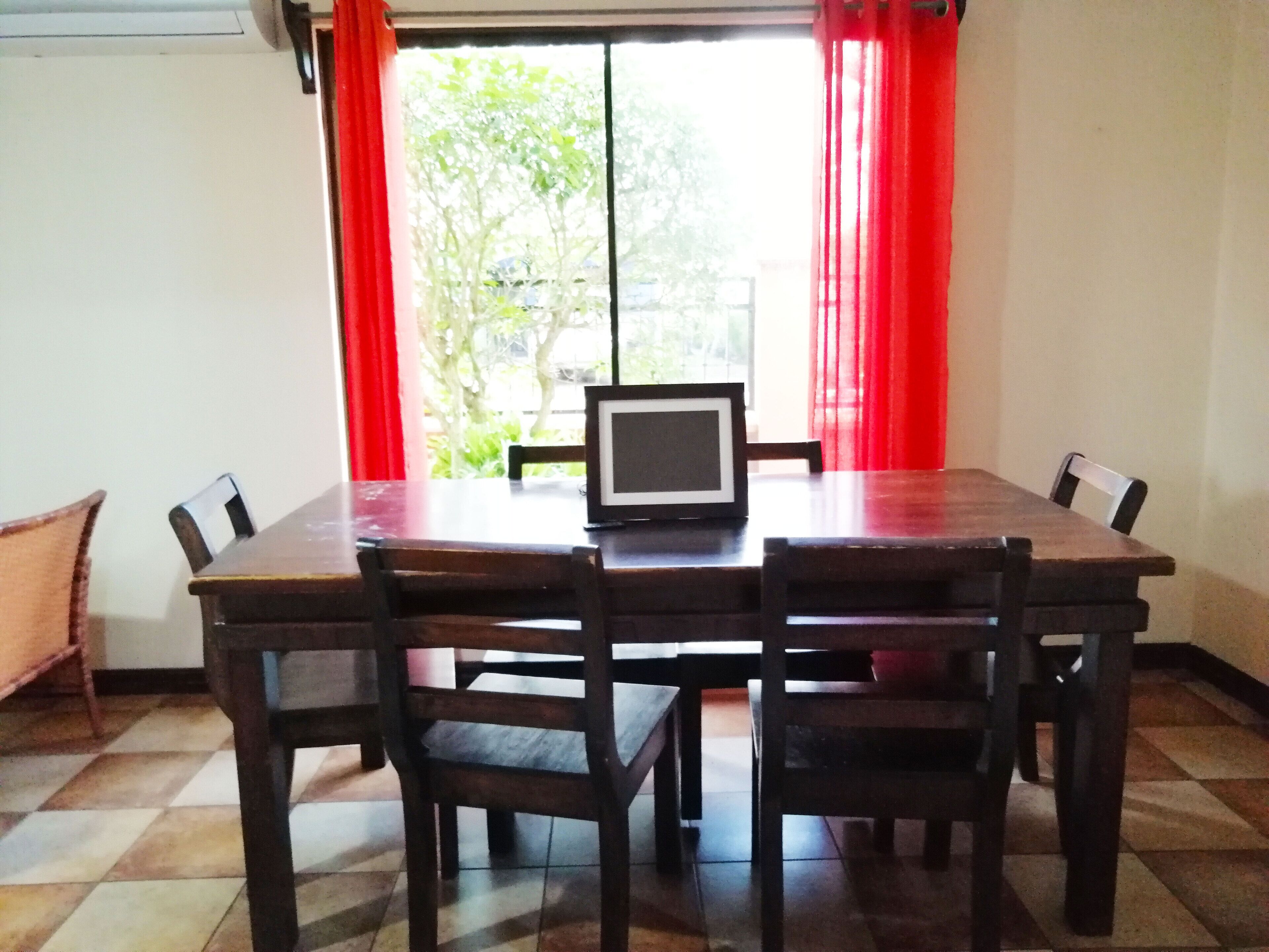 Un comedor con una mesa y sillas de madera, un televisor sobre la mesa y cortinas rojas.