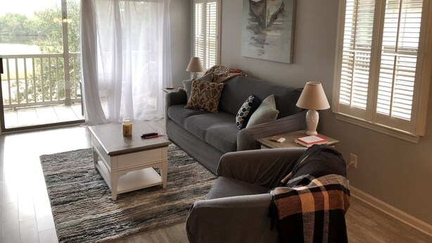 A living room with a grey sofa, a coffee table, a lamp, and a painting on the wall. - Relaxing Lake and Fairway view condo.        5 Star reviews. Clean and quiet. (Pawleys Island)