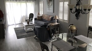 A living room with a sofa, a glass coffee table, a dining table with chairs, a ceiling fan, and a chandelier. - Relaxing Lake and Fairway view condo.        5 Star reviews. Clean and quiet. (Pawleys Island)