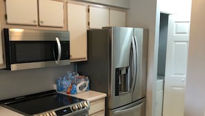 A modern kitchen with stainless steel appliances, including a microwave, refrigerator, stove, and oven. There is a white countertop and a wooden floor mat with text. - Relaxing Lake and Fairway view condo.        5 Star reviews. Clean and quiet. (Pawleys Island)