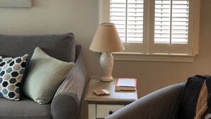 A living room with a grey sofa, a small side table with a lamp, and a window with blinds. - Relaxing Lake and Fairway view condo.        5 Star reviews. Clean and quiet. (Pawleys Island)
