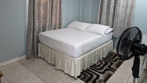 A bedroom with a bed, curtains, a fan, and a patterned rug. - Malay Getaway and taxi service (Laborie)