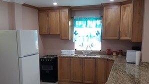 A kitchen with wooden cabinets, a white refrigerator, a stove, and a granite countertop. - Malay Getaway and taxi service (Laborie)
