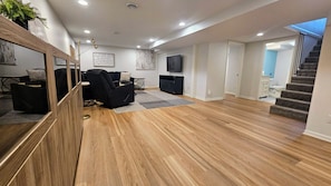 A spacious living room with a wooden floor, a black sofa, a TV, and a staircase leading to another level.