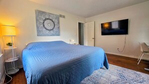 A bedroom with a large bed, a flat-screen TV mounted on the wall, and a bedside table with a lamp.