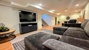 A modern living room with a flat-screen TV, dark sofas, a round coffee table, and a staircase leading to another level.