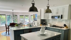 Une cuisine moderne dotée d’un grand îlot central, de meubles de rangement aux couleurs sombres, de plans de travail blancs et de luminaires suspendus.