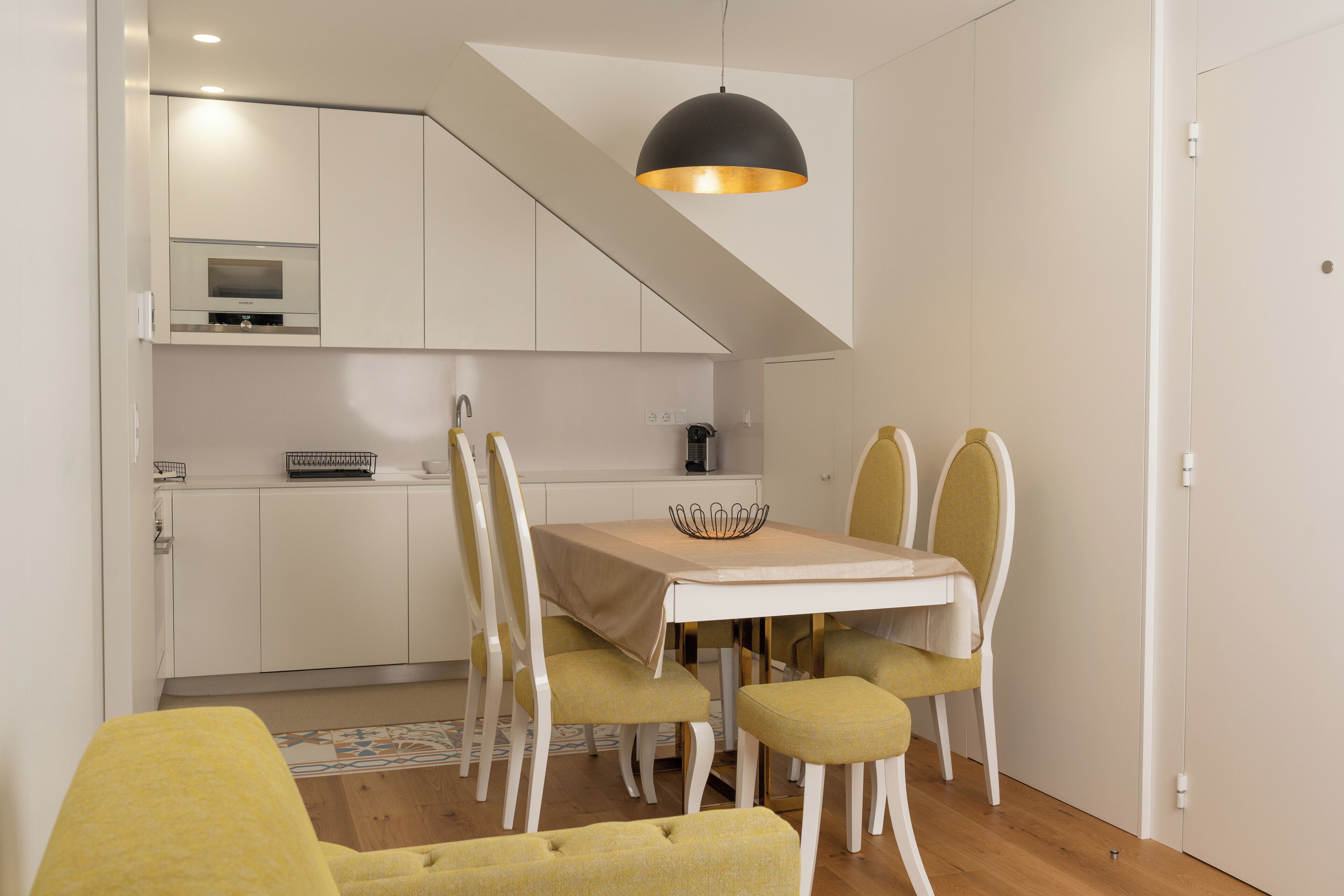 A modern kitchen with white cabinets, a built-in oven, and a dining area with a table and chairs.