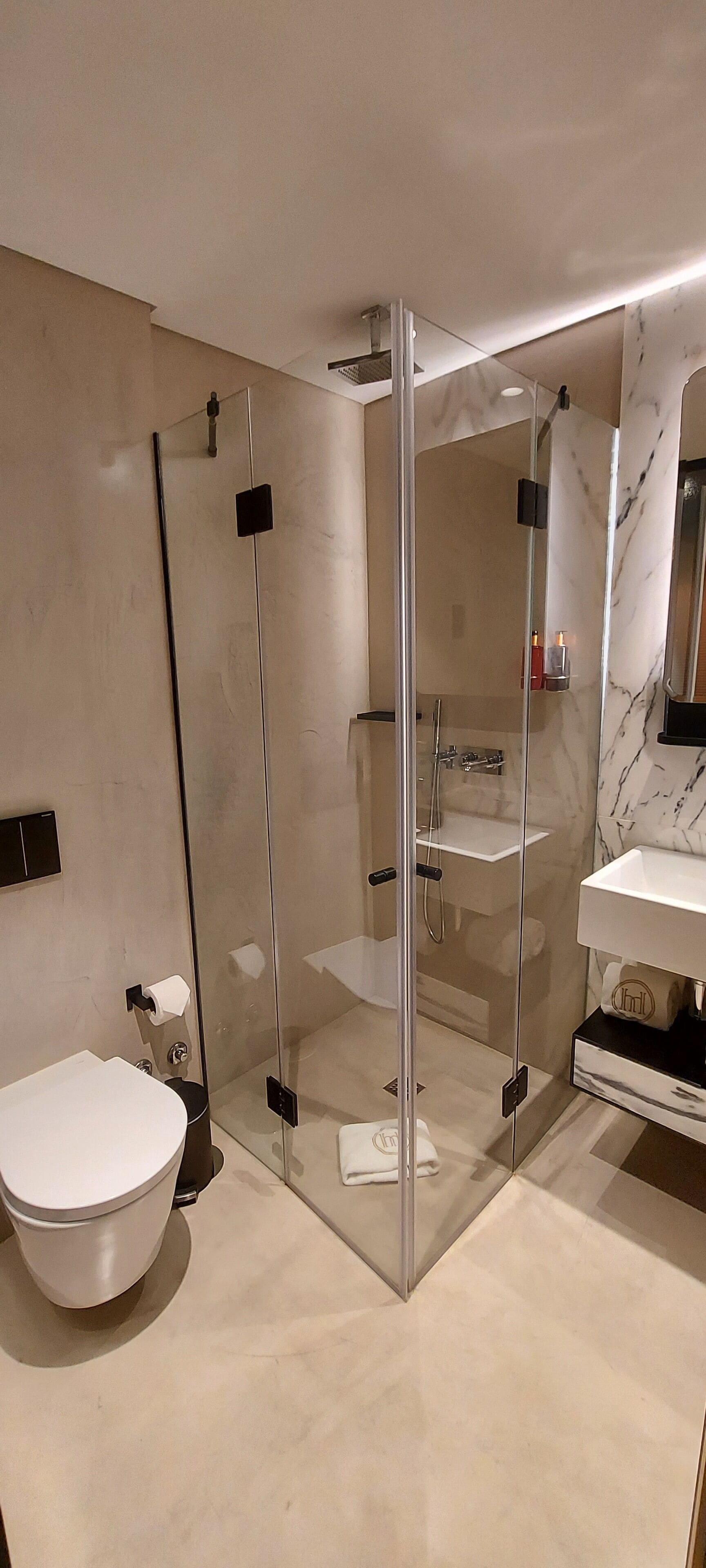 Une salle de bain moderne avec une douche à parois de verre, des toilettes blanches et un lavabo surmonté d’un plateau en marbre.