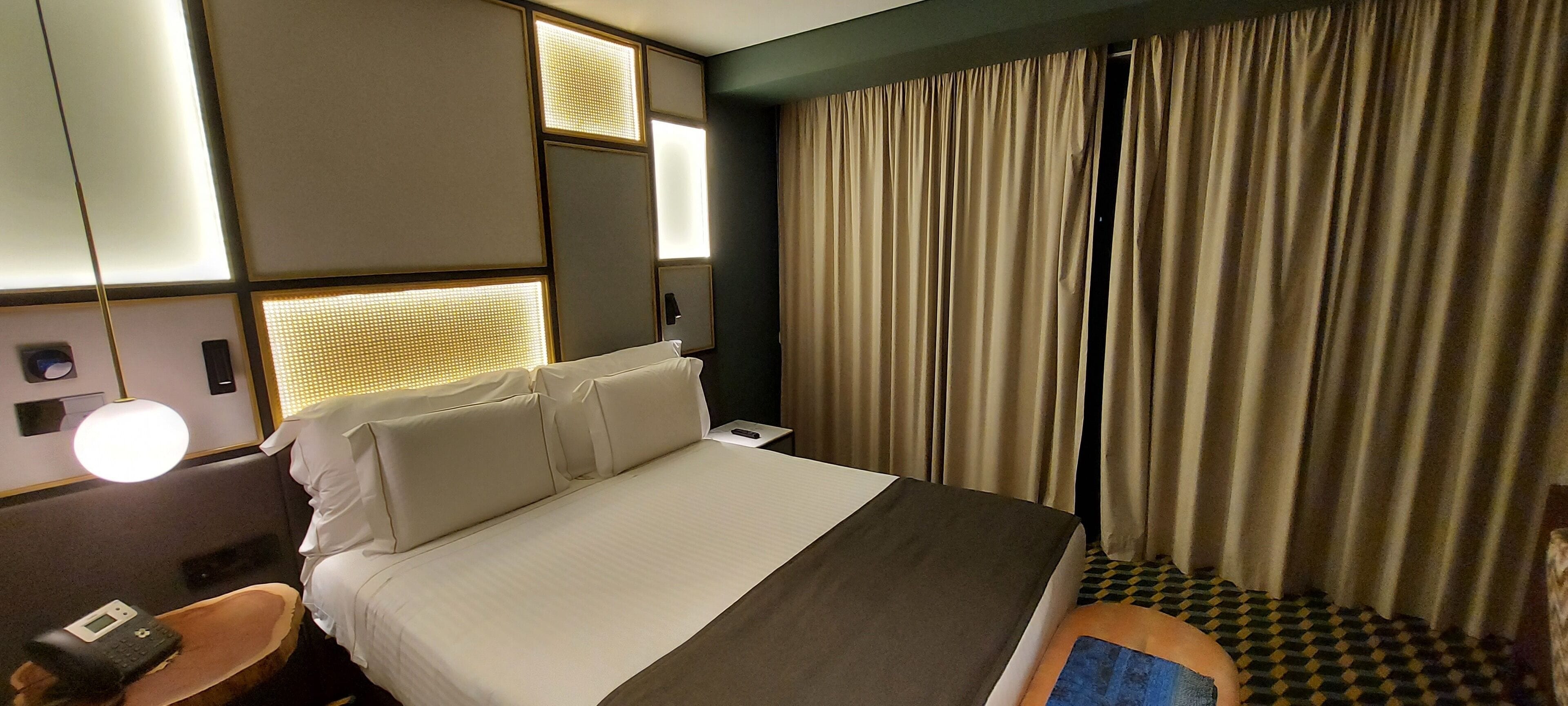 Ein Hotelzimmer mit Bett, Nachttisch, Lampe und Vorhängen.