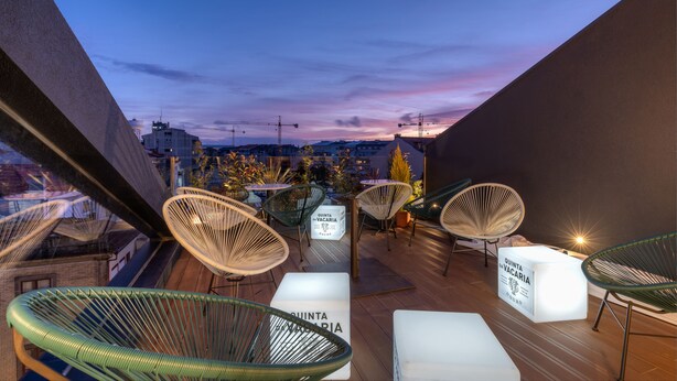 Una terrazza sul tetto con sedie in vimini e tavoli bianchi, con un cartello che riporta la scritta 'QUINTA DA VACARIA'.