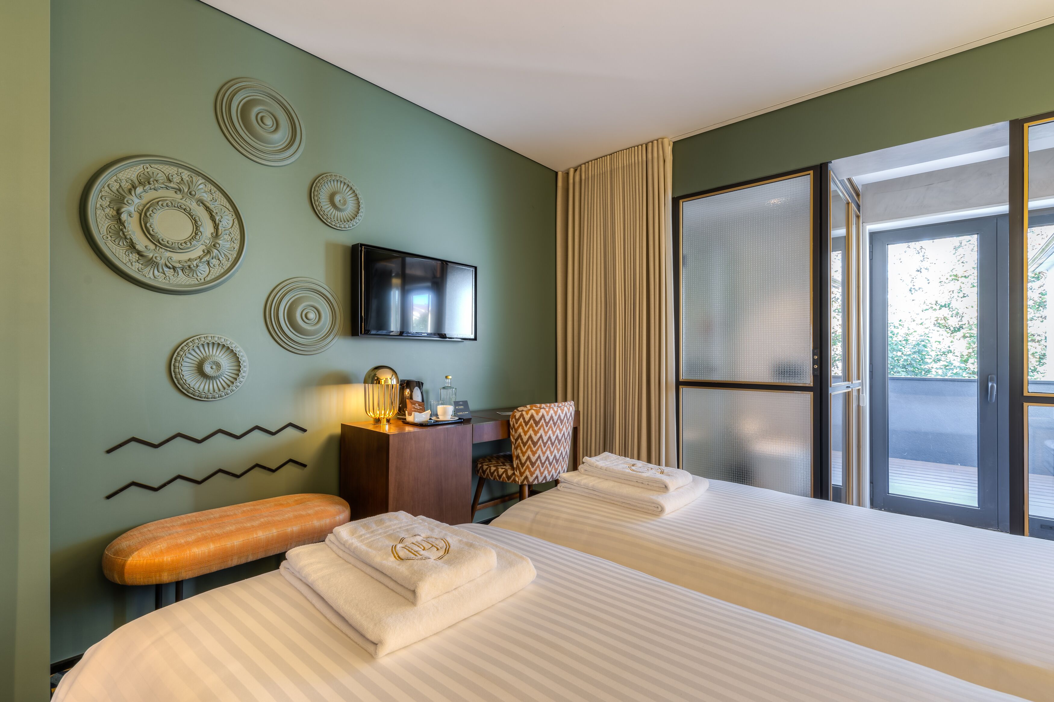 A hotel room with two beds, a desk, a television, and decorative wall art.