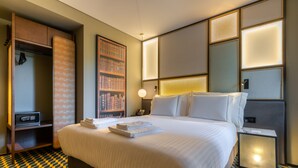 Una camera d'albergo con un letto grande, un armadio, una libreria e un comodino con una lampada.