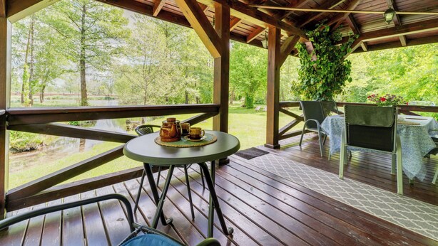 Un espacio al aire libre cubierto con terraza de madera, una mesa con sillas y vistas a un paisaje verde.