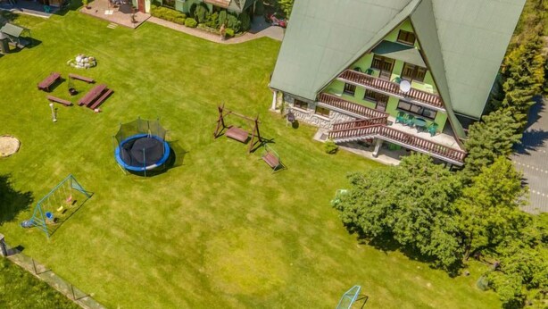 Et moderne hus med en stor græsplæne, trampolin og gyngestativ.
