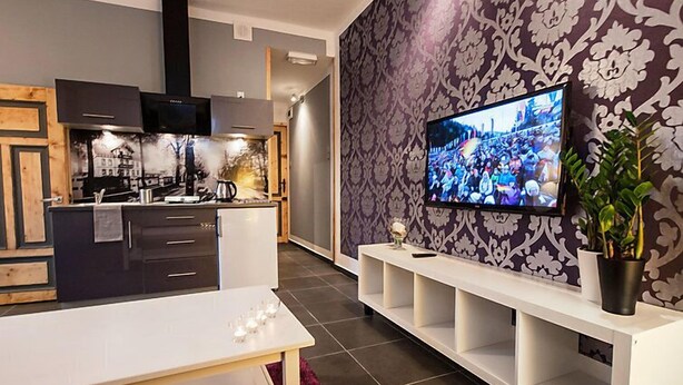 A modern kitchen with a central island, a dining area with a white table, and a TV mounted on a patterned wall. - Apartment Fiolet by Interhome (Szczawno Zdroj)