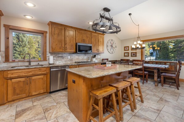 A kitchen with wooden cabinets, a central island with stools, a built-in microwave, and a large window overlooking trees.
