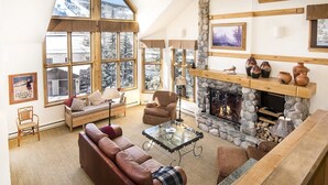Una sala de estar acogedora con chimenea de piedra, ventanas amplias y un techo alto.