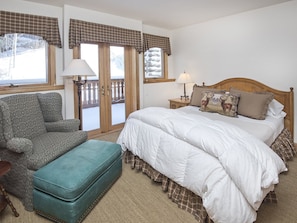 A bedroom with a bed, a chair, a bench, and a view of the outside through a door. - Meadows Townhome (Avon)