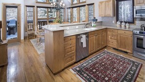 A spacious kitchen with wooden cabinets, a granite countertop, and a large island. There are multiple windows providing natural light and views of the outdoors. - Meadows Townhome (Avon)