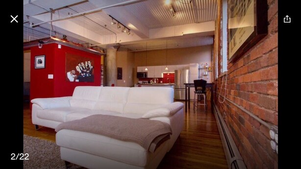 Ein modernes Wohnzimmer mit einem weißen Sofa, einer roten Akzentwand und einer Küche im Hintergrund.