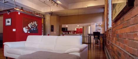A modern living room with a white sofa, a red accent wall, and a kitchen in the background.