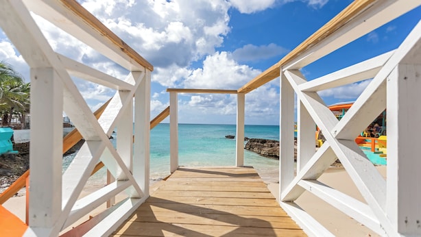 A wooden deck leading to a beach with clear turquoise water and a rocky shoreline. - Maho Beach House - Spacious 1 Bedroom Suite (Maho, Sint Maarten)