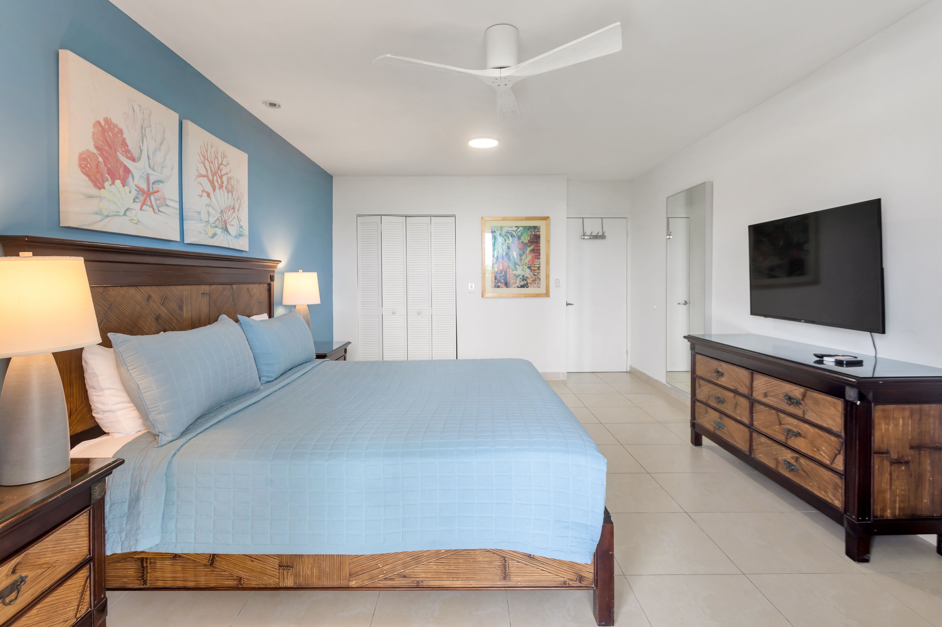 A bedroom with a bed, bedside lamps, a dresser, a TV, and artwork on the walls.