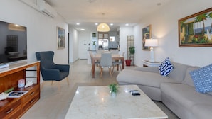A modern living room with a TV, sofa, coffee table, and dining area. - Maho Beach House - Spacious 1 Bedroom Suite (Maho, Sint Maarten)