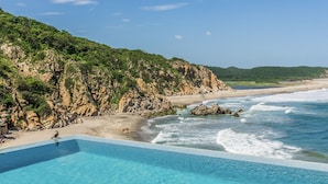 A beach with a clear blue pool and rocky cliffs. - Oceanfront Luxury Property in Elite Development (Huatulco)