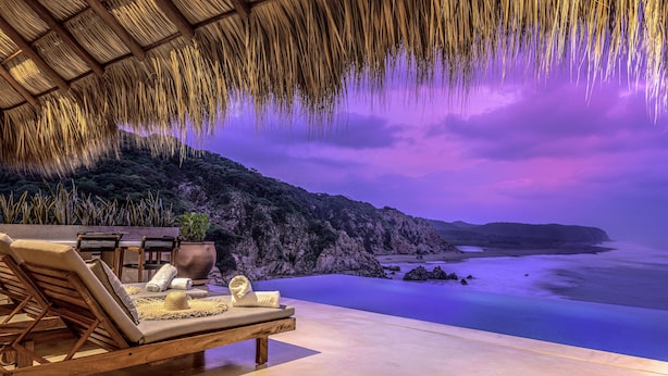 A beachside lounge with a thatched roof, lounge chairs, and a view of the ocean. - Oceanfront Luxury Property in Elite Development (Huatulco)