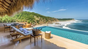A poolside area with lounge chairs, a table, and a view of the ocean. - Oceanfront Luxury Property in Elite Development (Huatulco)