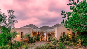 A resort with thatched-roof structures, lush greenery, and a serene evening ambiance. - Oceanfront Luxury Property in Elite Development (Huatulco)
