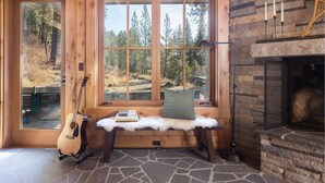 Ein gemütliches Blockhaus-Interieur mit Kamin aus Stein, einer Bank mit einem Buch und einer Gitarre, die an der Wand lehnt.
